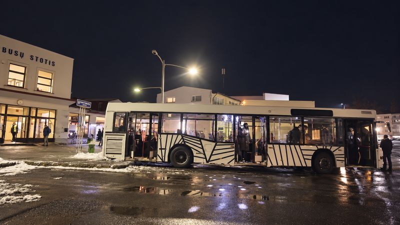 A white bus with black stripe graphics at a bus station at night, doors open, people inside