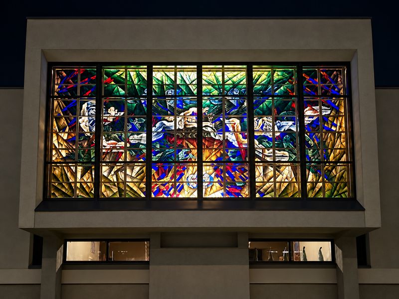 A stained-glass window lit at night in a concrete facade