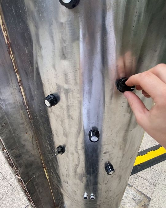 A hand turning a black knob set into a steel pipe